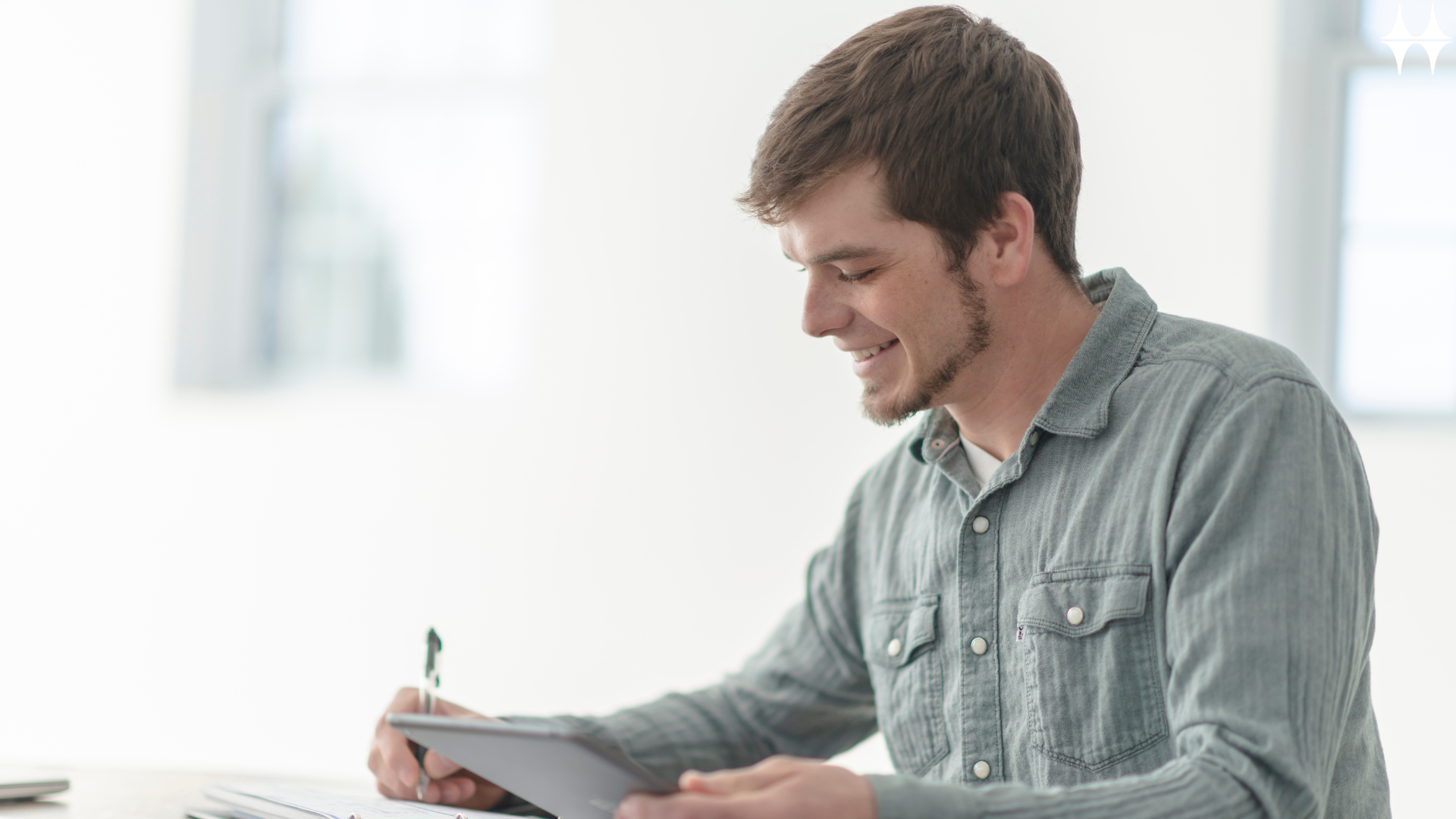 Ein Mann sitzt am Tisch und hält ein Blatt Papier und einen Stift in der Hand