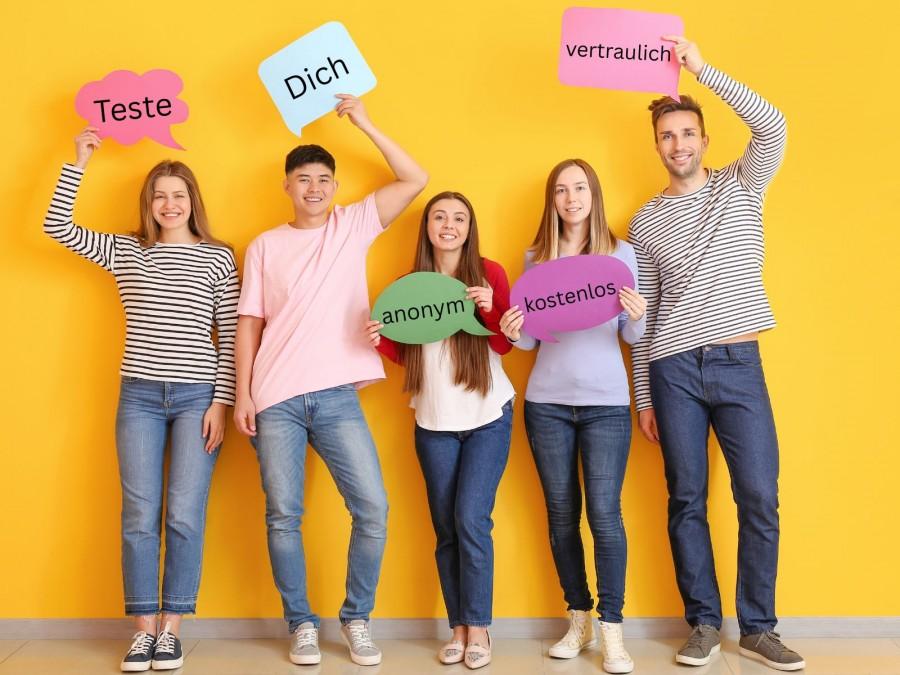 Drei junge Frauen und zwei junge Männer halten Schilder in die Kamera mit den Worten: Teste Dich anonym, kostenlos, vertraulich.