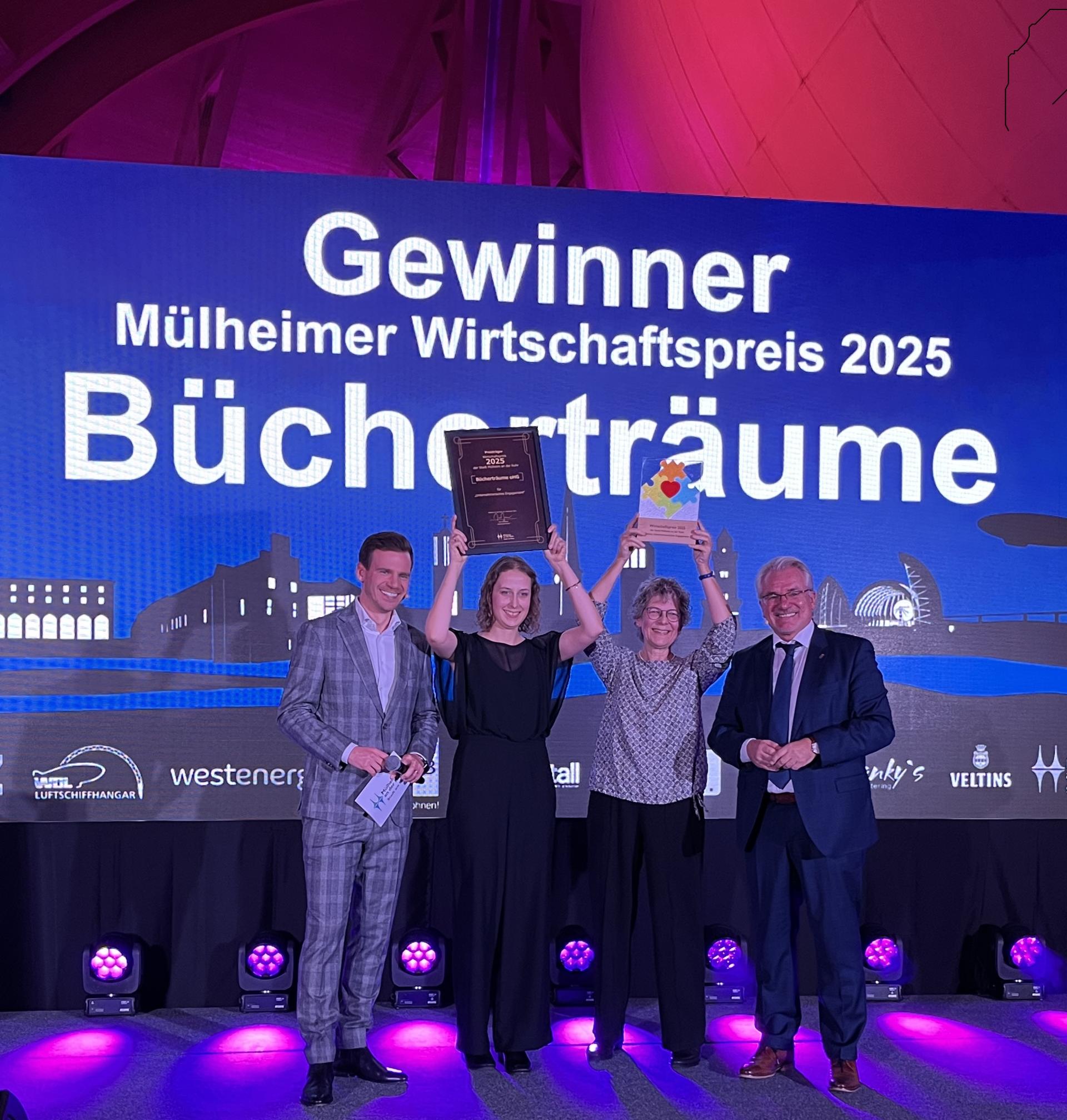 Vier Personen stehen auf der Bühne. Die beiden Damen in der Mitte halten ihre Urkunde und den Wirtschaftspreis in die Höhe.
