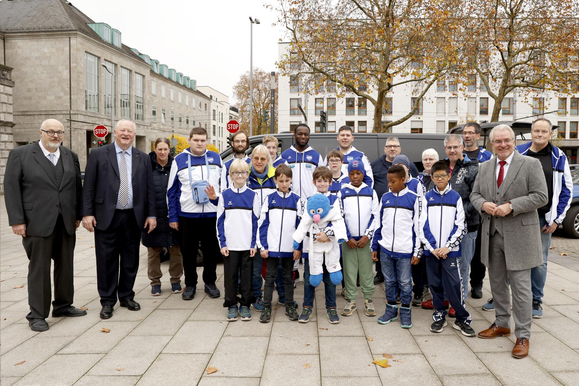 Auf dem Rathausmarkt hat sich eine Gruppe Judoka - Kinder verschiedenen Alters in blau-weißer Trainingsgarderobe - aufgestellt, zusammen mit dem Oberbürgermeister, ihrem Trainer, Begleitenden und Politikern.