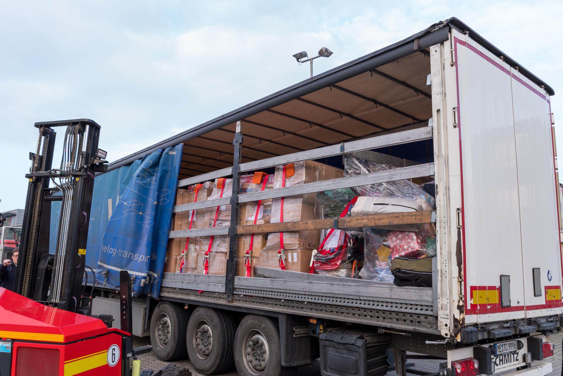 Offener Lkw-Anhänger mit Weihnachtspaketen und verpackten Hilfsgütern für die ukrainische Stadt Ivano-Frankivsk, daneben ein roter Gabelstapler.