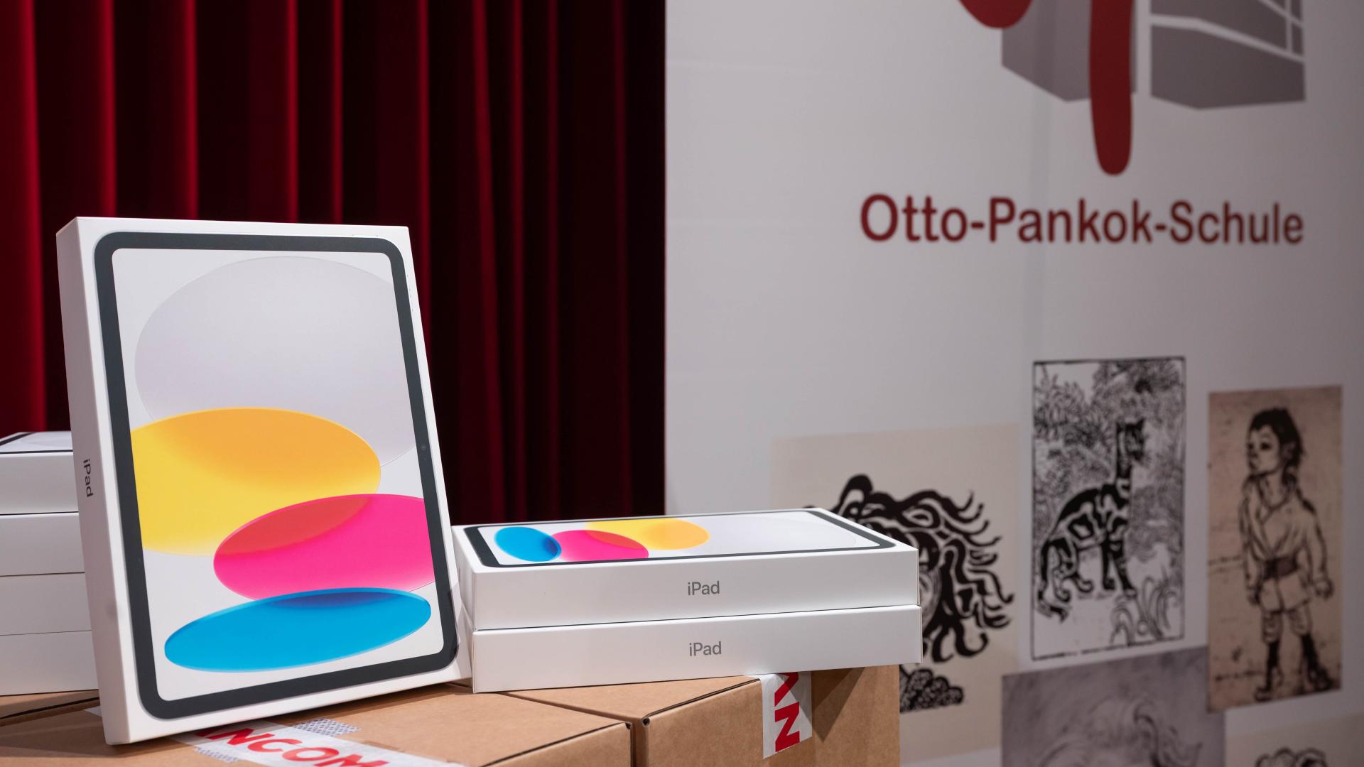 iPads liegen auf einem Tisch, im Hintergrund ist ein Banner mit der Aufschrift "Otto-Pankok-Schule" zu sehen
