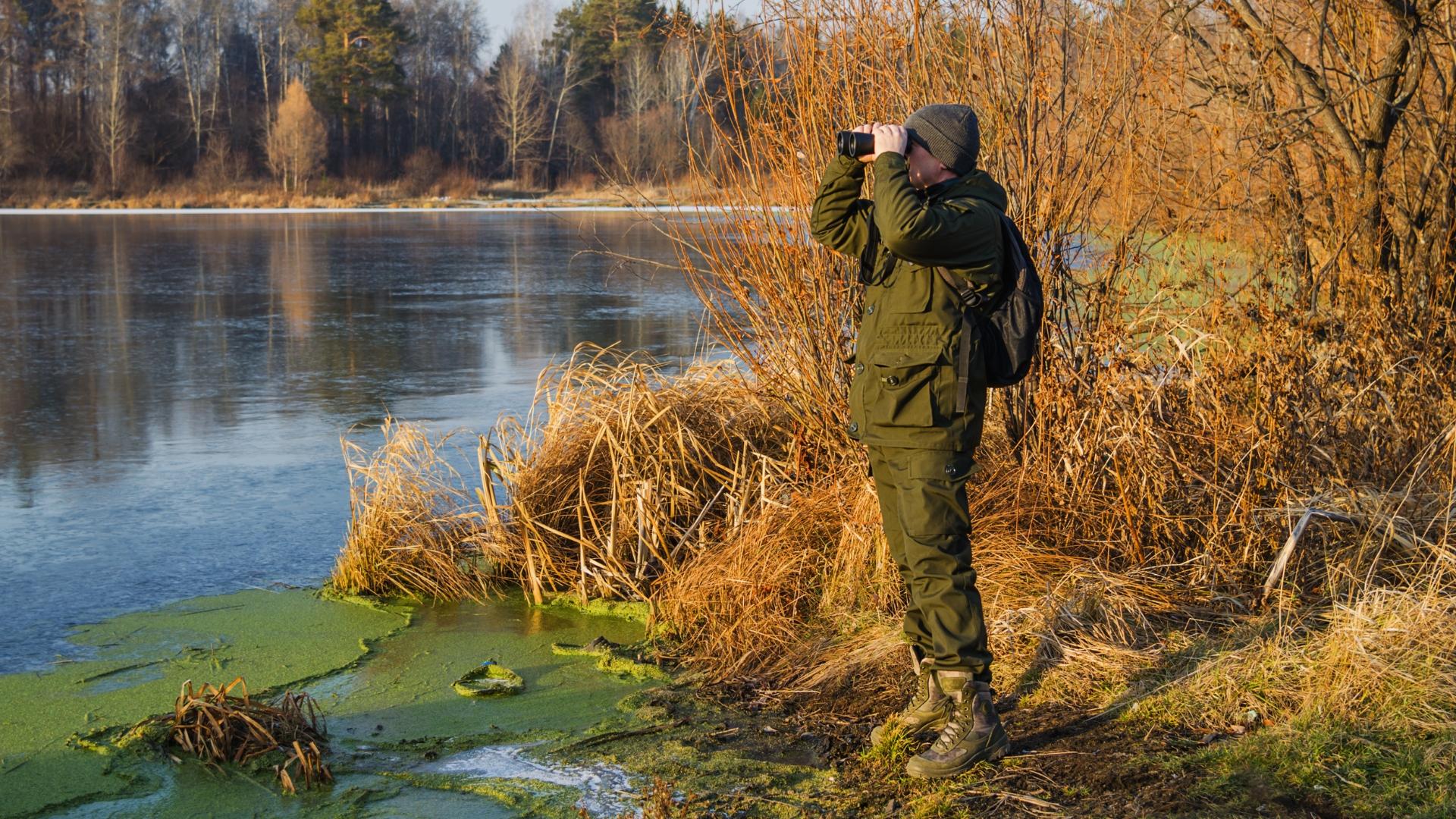 Jäger steht mit einem Fernglas an einem See