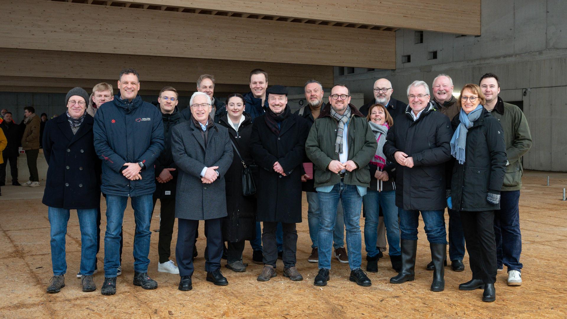 Gruppe von Menschen in Winterkleidung steht im Rohbau einer Schwimmhalle mit Betonwänden.