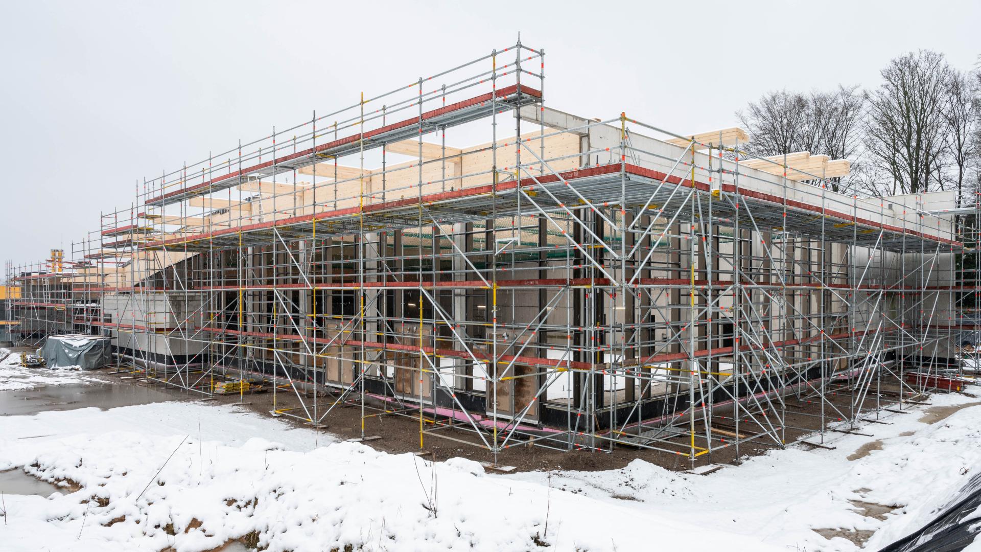 Rohbau eines eingeschossigen Gebäudes mit Gerüst auf schneebedecktem Baugrund