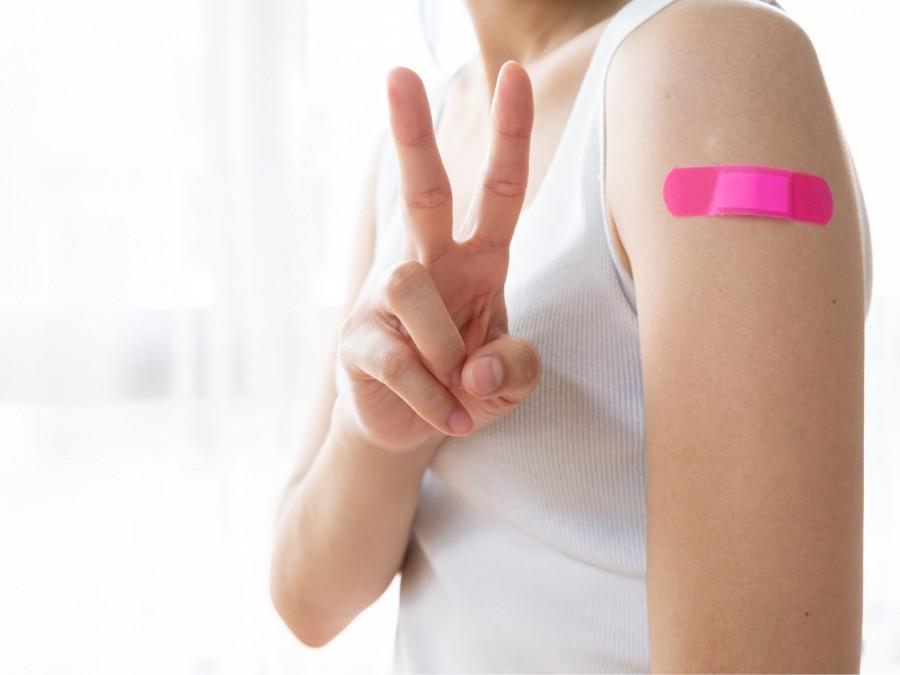 Eine junge Frau mit einem weißen Shirt wurde geimpft. Auf Ihrem Oberarm befindet sich ein pinkes Pflaster.