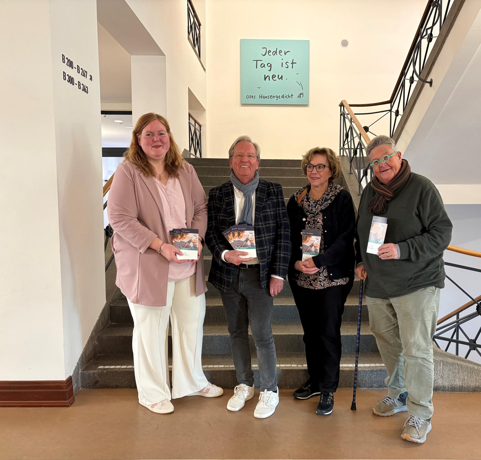 Vier Personen stehen in einem Treppenhaus und halten Dokumente in der Hand.