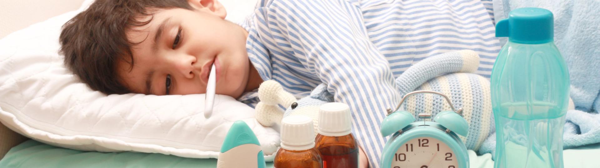 Ein kranker Junge liegt mit einem Fieberthermometer im Bett.