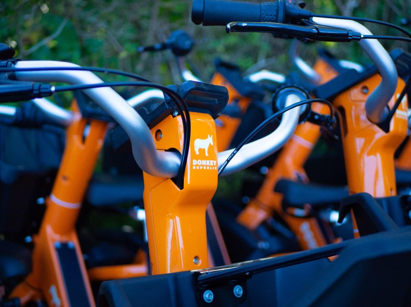 abgestellte Fahrräder des dänischen Bike-Sharing-Spezialist Donkey Republic, Nahaufnahme Lenker mit Logo, orangene Bikes mit Esel Logo