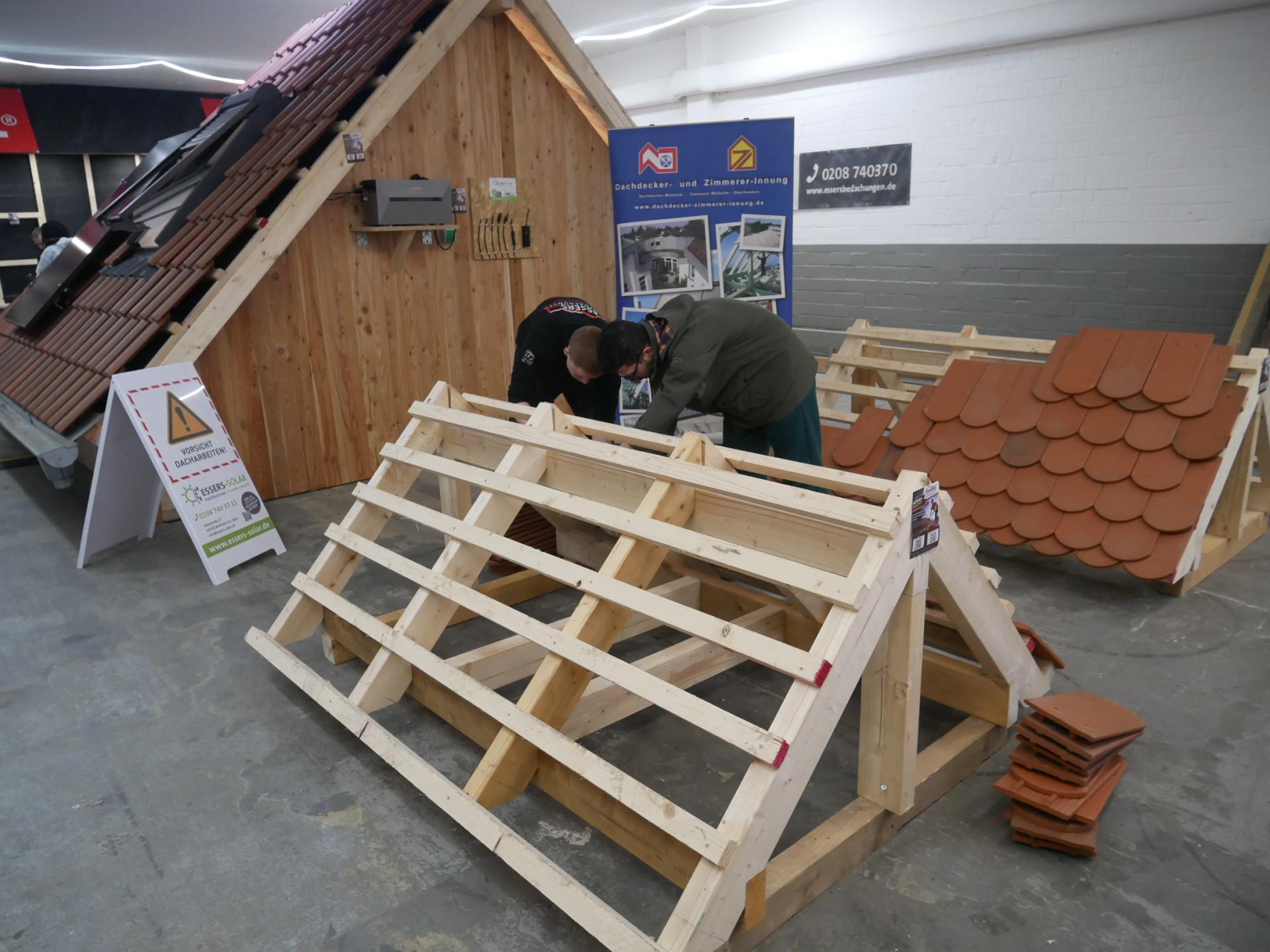 In einer Lehrwerkstatt können Jugendliche sich an einem Holzgerüst, das einem kleinen Spitzdach nachempfunden ist, mit Schindeln im Dachdecken ausprobieren.