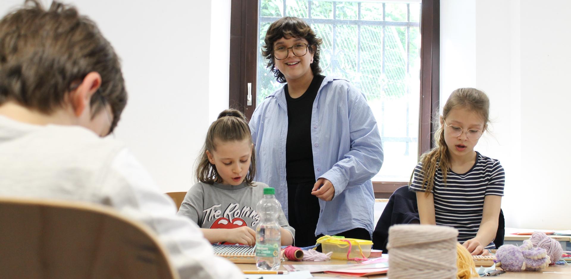 Das Foto zeigt die Künstlerin Maria Reneé Morales Garcia umgeben von Kindern während eines Workshops in der Malschule.