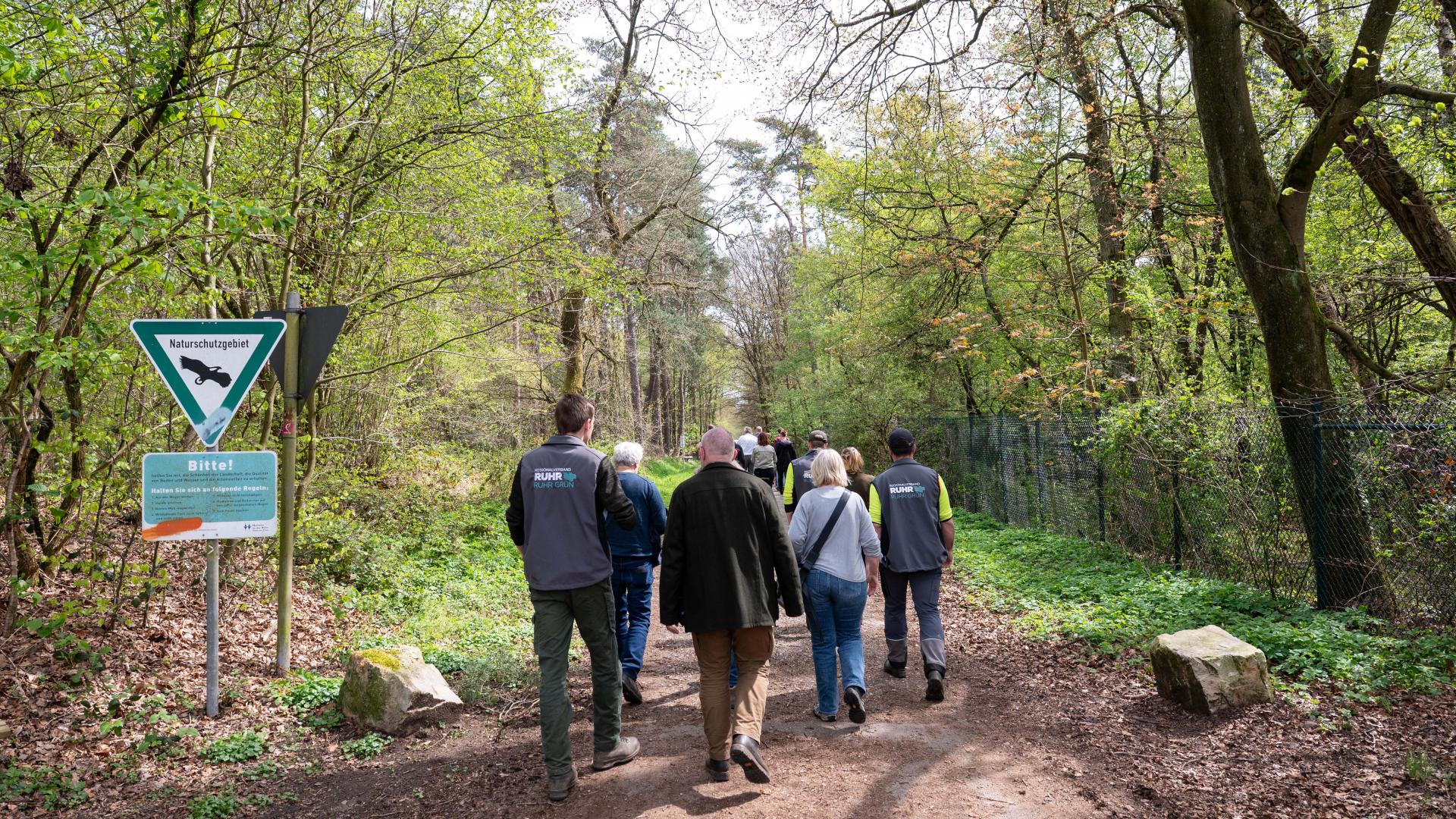Gruppe von Menschen geht auf einem Waldweg mit Schildern am linken Wegesrand im Mülheimer Stadtwald