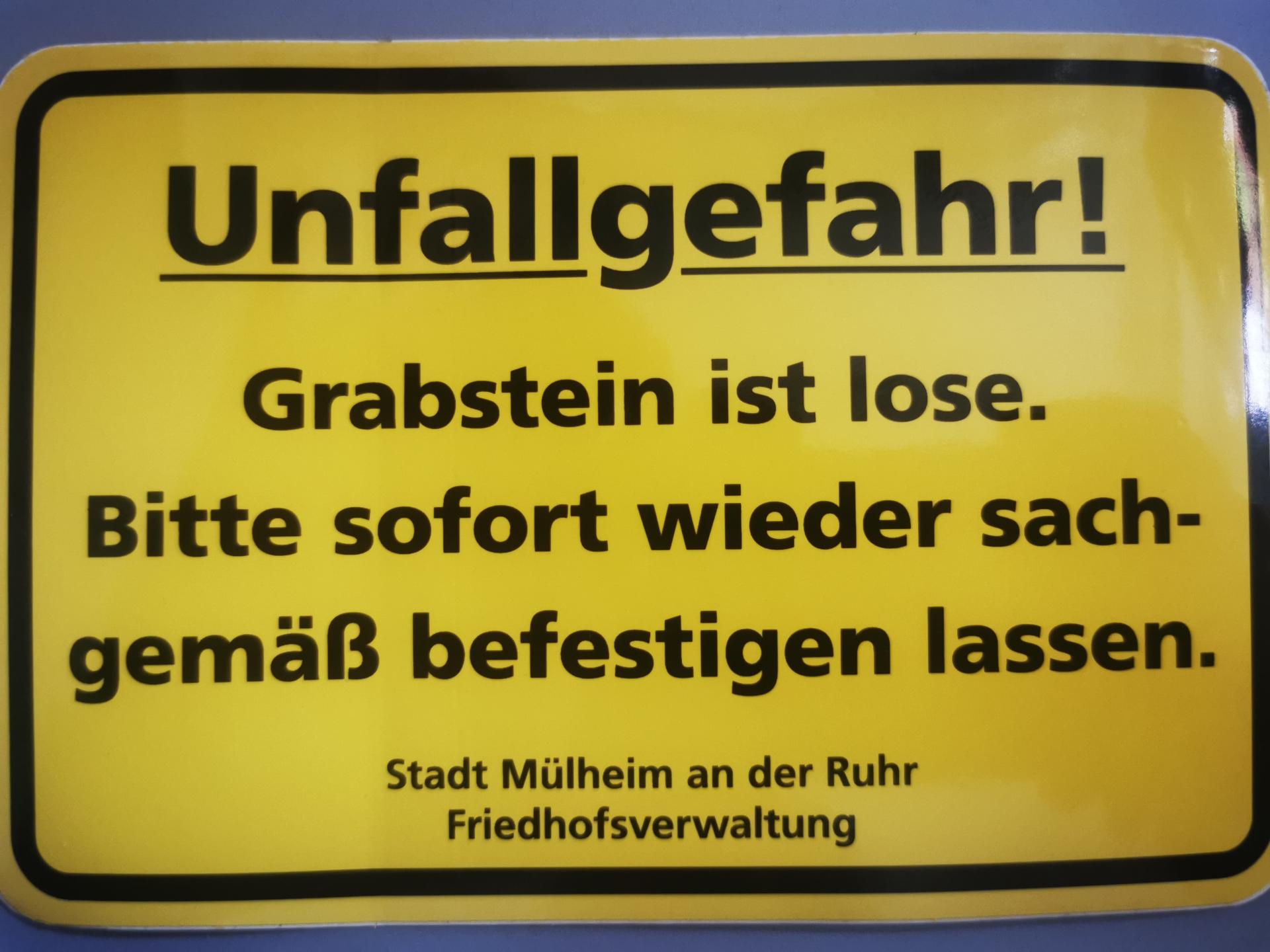 Ein gelber Hinweis-Aufkleber, der darauf hinweist, dass ein Grabstein lose ist.