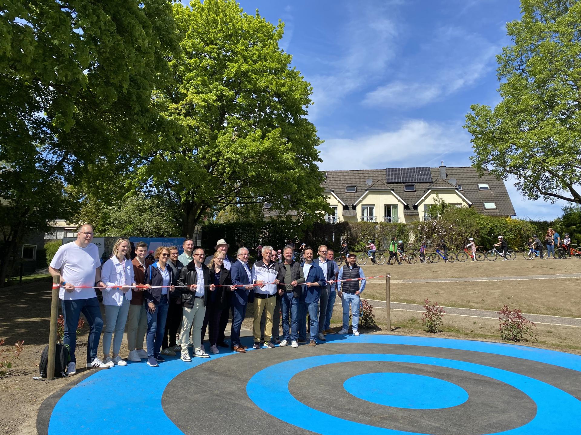 Eine Gruppe von Personen aus Vertreterinnen und Vertretern von Stadt, Mülheimer SportService, Sportbund e.V. und Politik stehen vor einem Band zur Eröffnung des Radmotorikparks