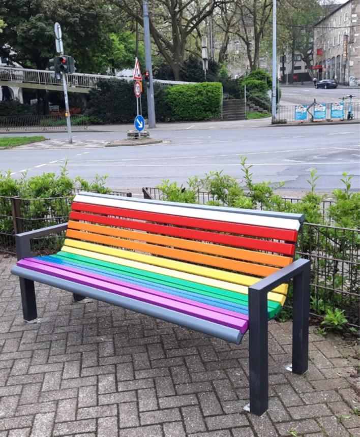 Aufstellung einer Sitzbank in Regenbogenfarben auf dem Regenbaumplatz vor dem Forum im Sommer 2025