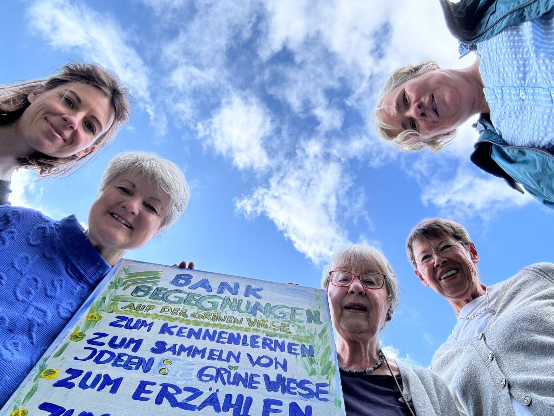 Fünf Frauen stehen um ihr Einladungsplakat für die Nachbarschaftswoche