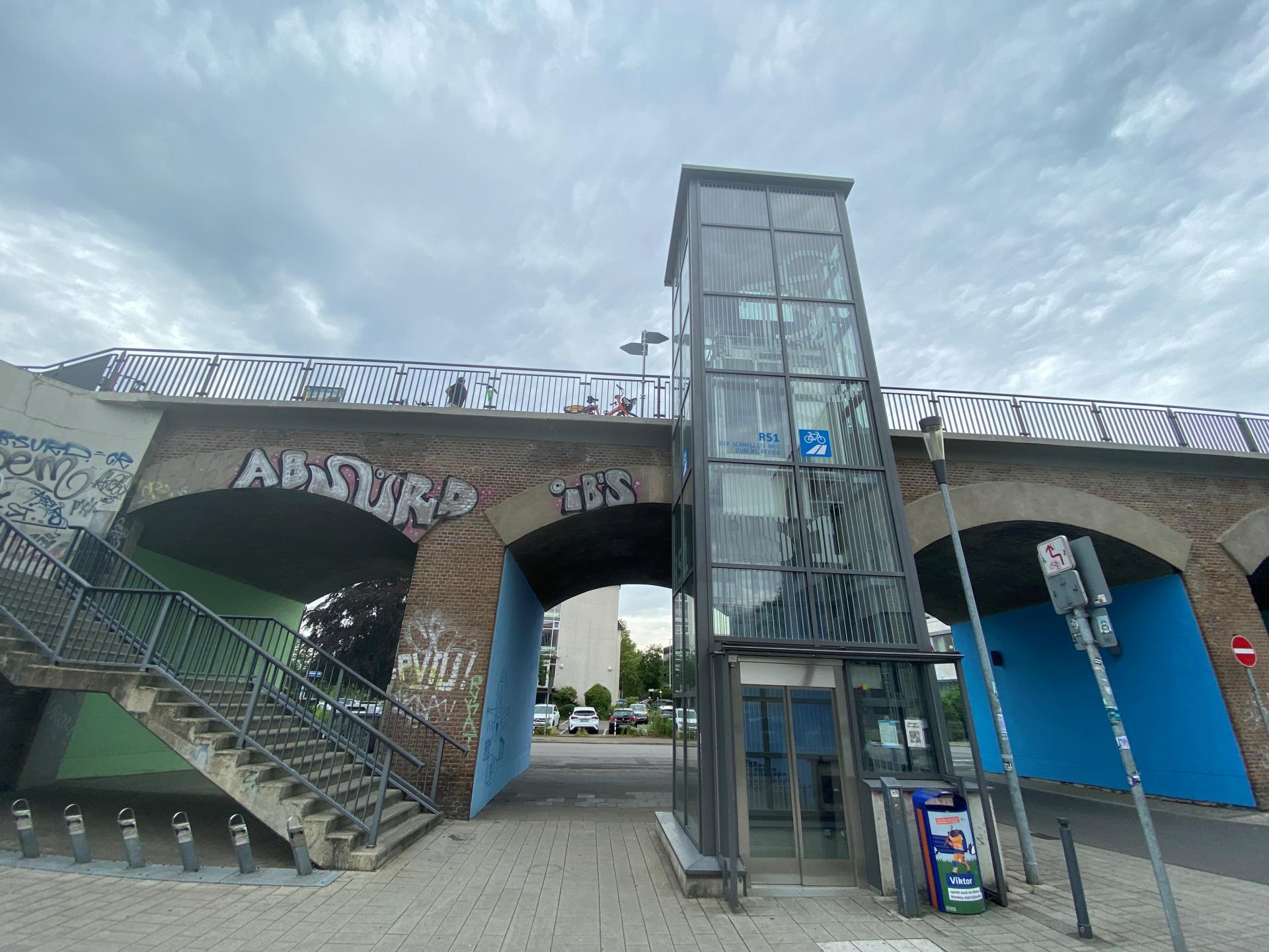 Auf dem Foto ist der Aufzug zum Radschnellweg RS1 abgebildet. Im Hintergrund ist eine Brücke, sowie der Treppenaufgang zu sehen.