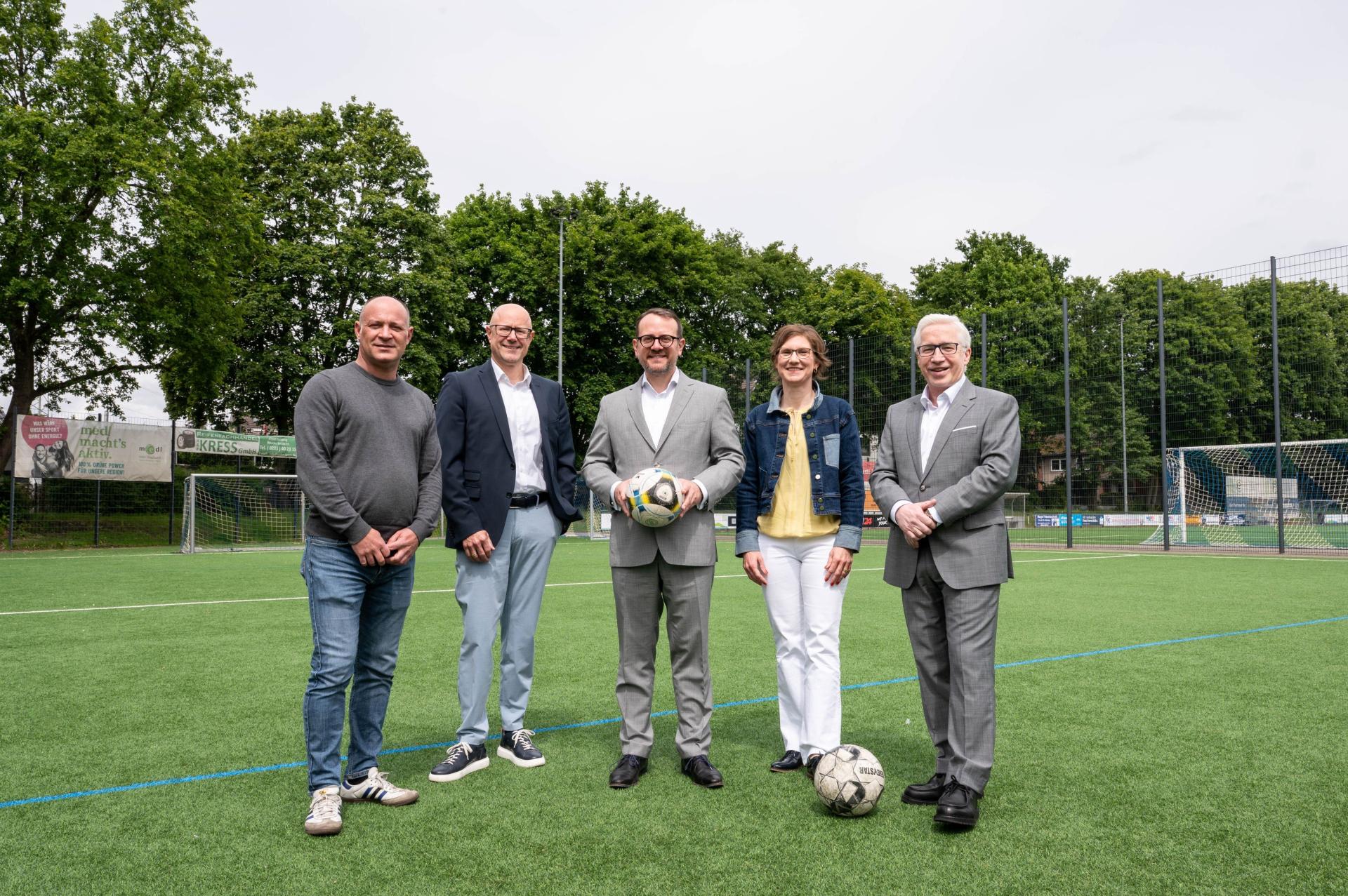 Fünf Personen stehen auf dem Rasen einer Sportanlage.