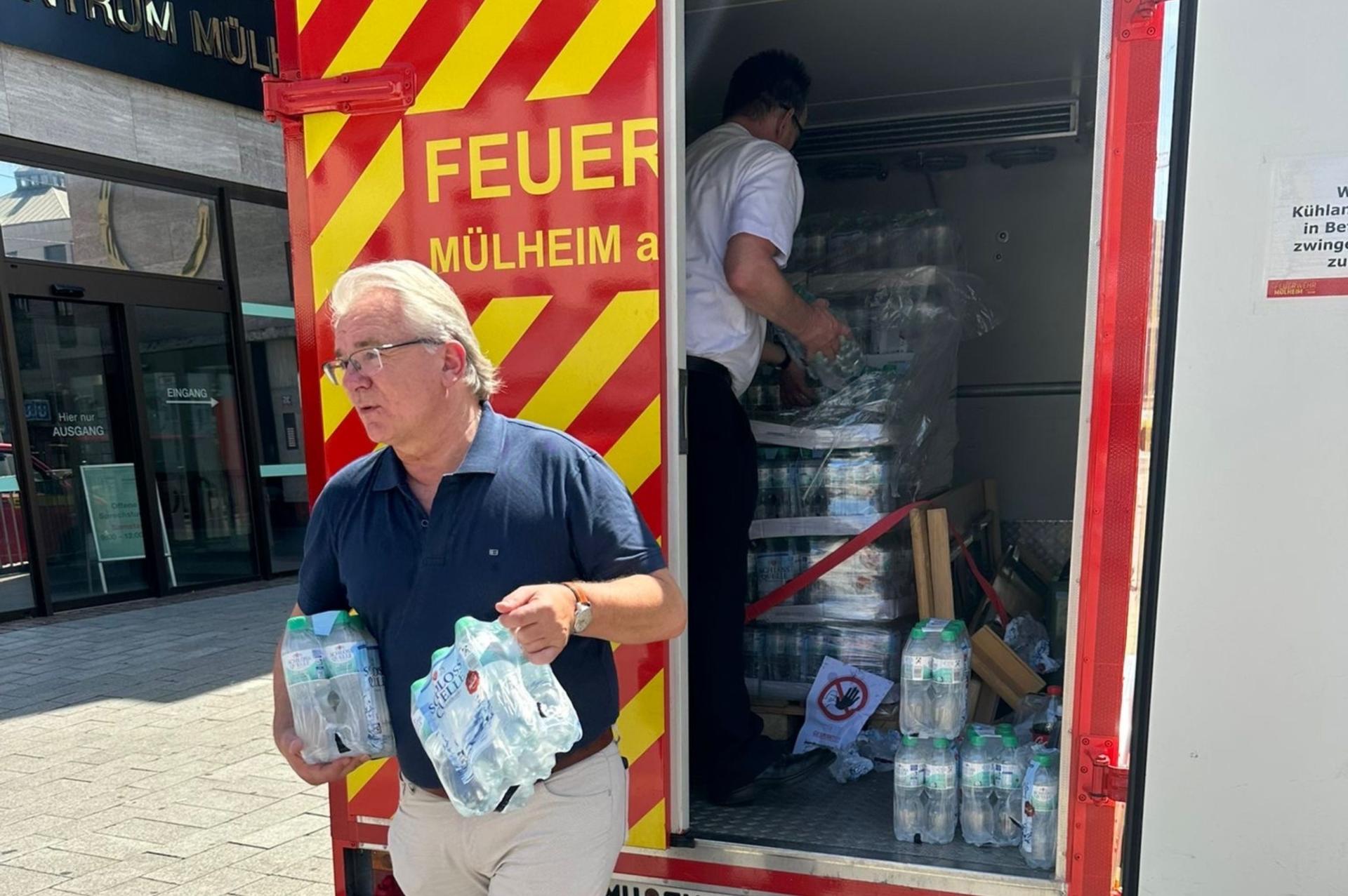 Der Oberbürgermeister holt zwei Träger mit Wasserflaschen aus dem Kühlwagen der Feuerwehr. Im offenen Wagen packt der Feuerwehrchef die Träger von einer Palette.