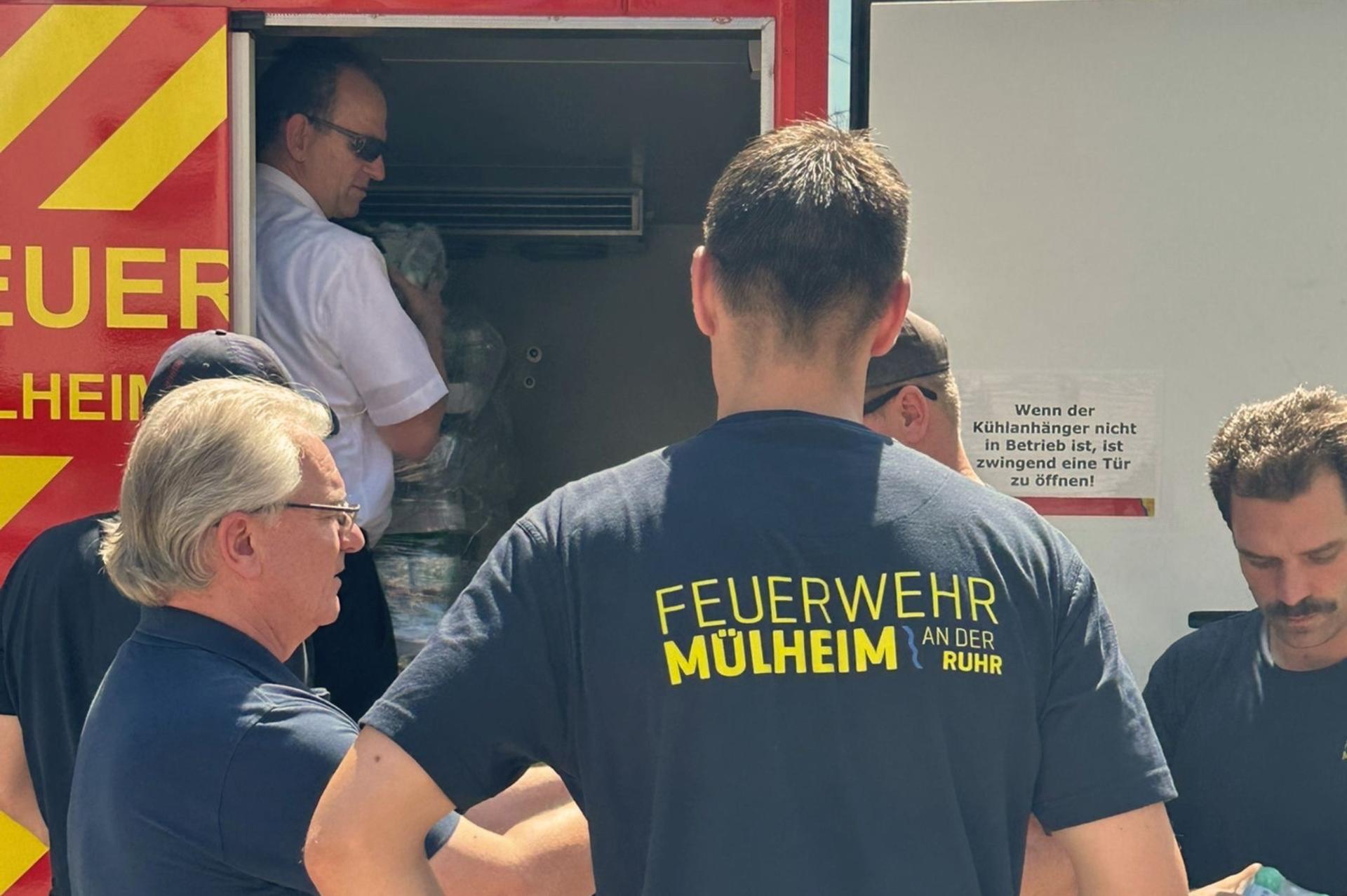 Der Oberbürgermeister steht zusammen mit einigen Feuerwehrleuten am geöffneten Kühlwagen der Feuerwehr. 