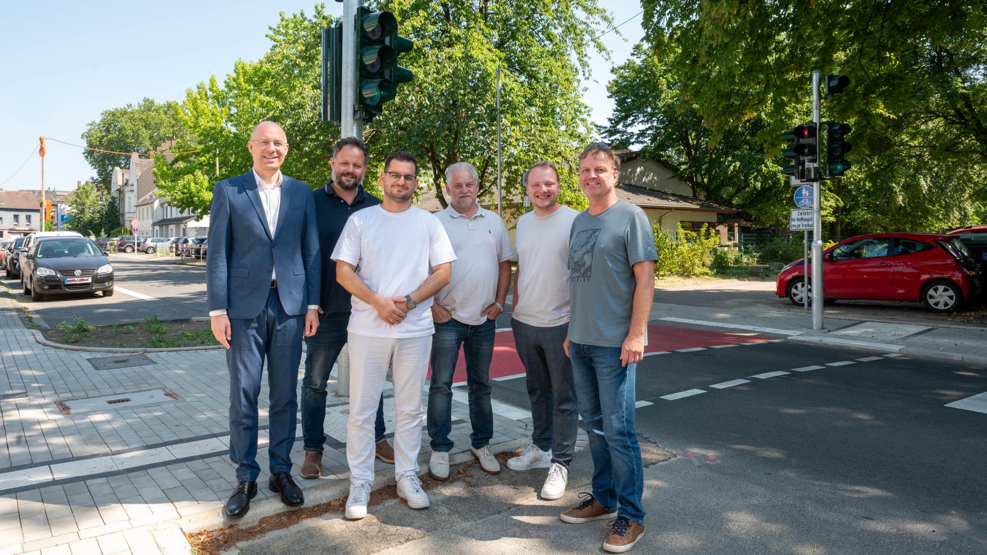 Gruppenfoto mit sechs Männern an neuer Ampelanlage auf der Kaiser-Wilhelm-Straße, im Hintergrund Autos und Bäume