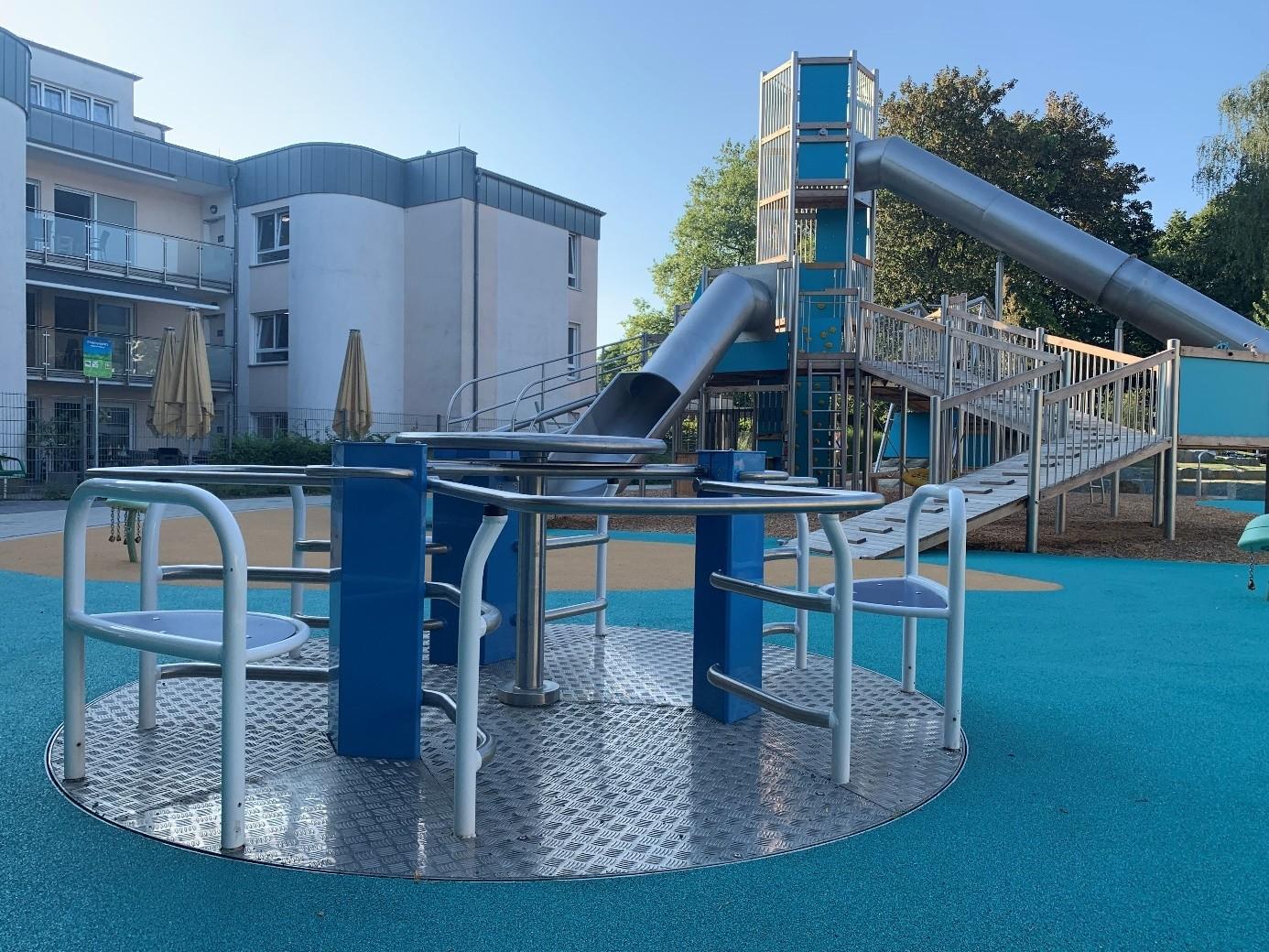 Auf dem Spielplatz ist ein ebenerdiges inklusives Karussell installiert worden. Es besteht aus einer Metallscheibe im Boden, Sitzen und Geländern beziehungsweise Möglichkeiten, sich festzuhalten.
