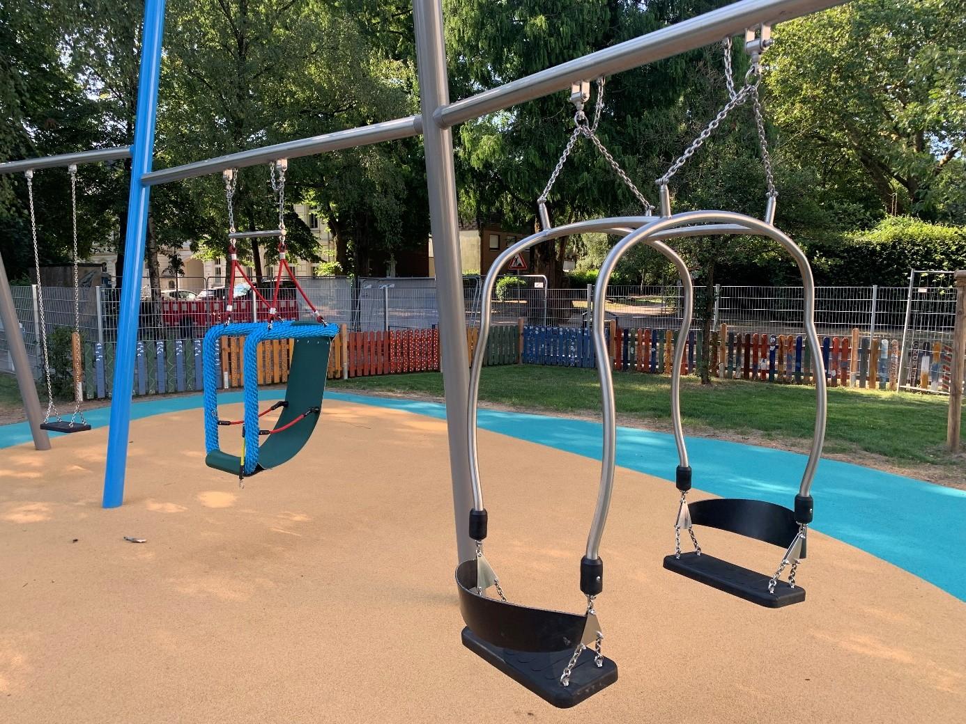 Der Spielplatz bietet drei verschiedene Schaukeln. Auf dem Bild eine Zweisitzer-Schaukel, eine Schaukel mit Rückenlehne und Rahmen und eine übliche Schaukel, bei der ein Schaukelbrett an zwei Ketten befestigt ist.