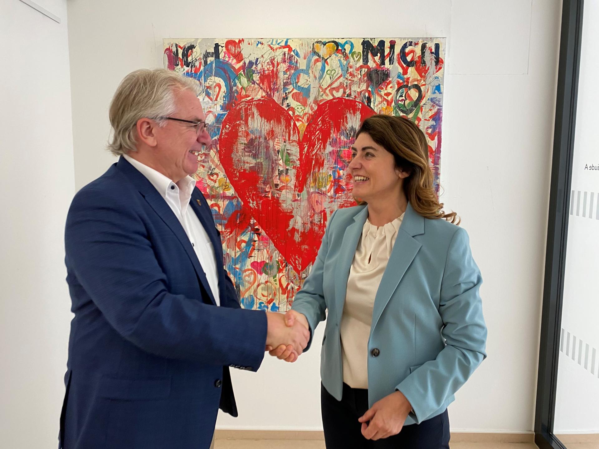 Vor einem Gemälde mit einem Herz schütteln sich ein Mann und eine Frau die Hand.