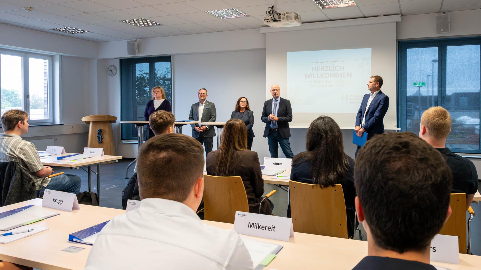 Mehrere Personen sitzen in der Feuerwehrschule und hören vier stehenden Personen zu, die vorne sprechen