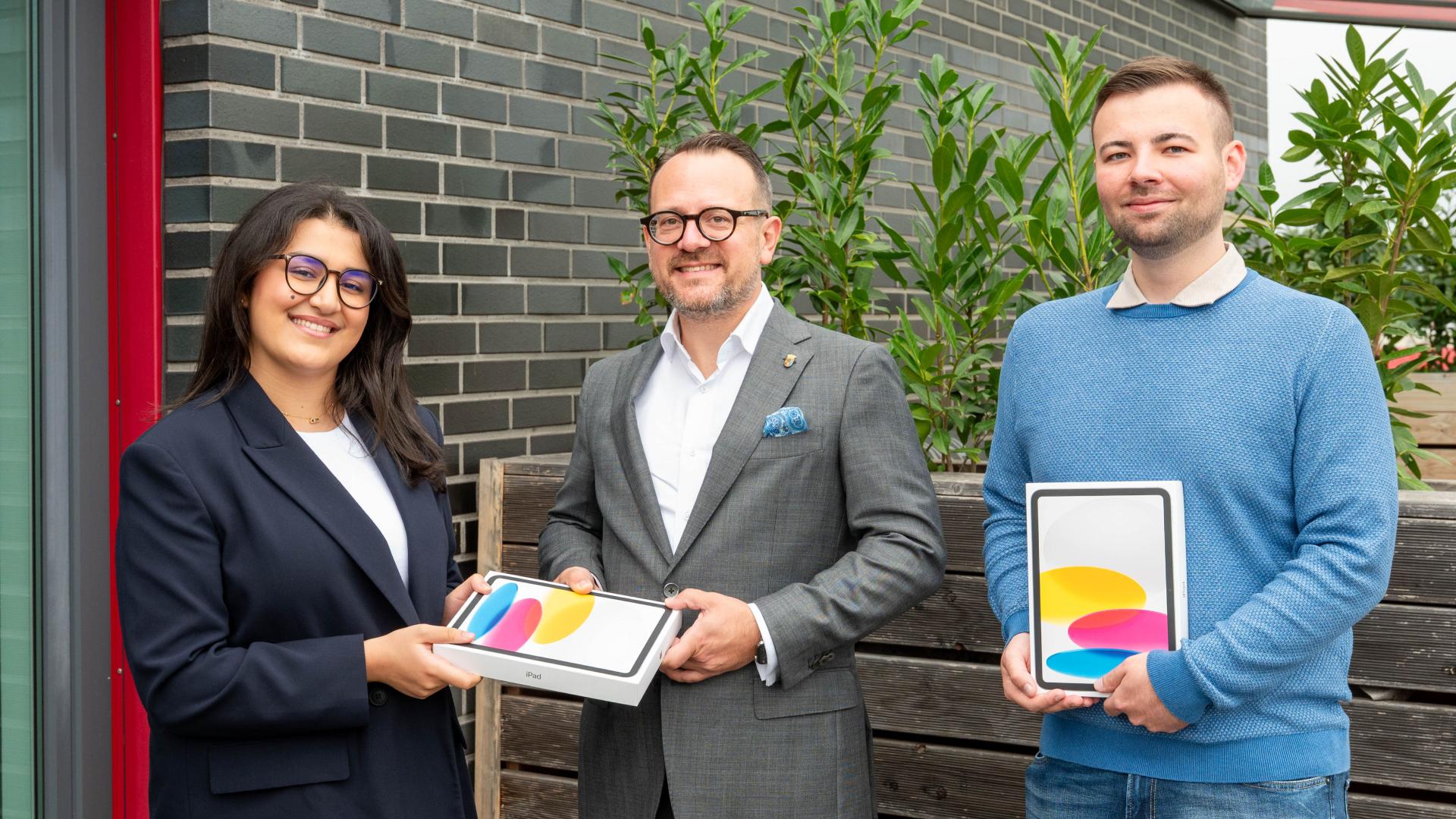 Stadtdirektor David Lüngen übergibt zwei Tablets an zwei Auszubildende