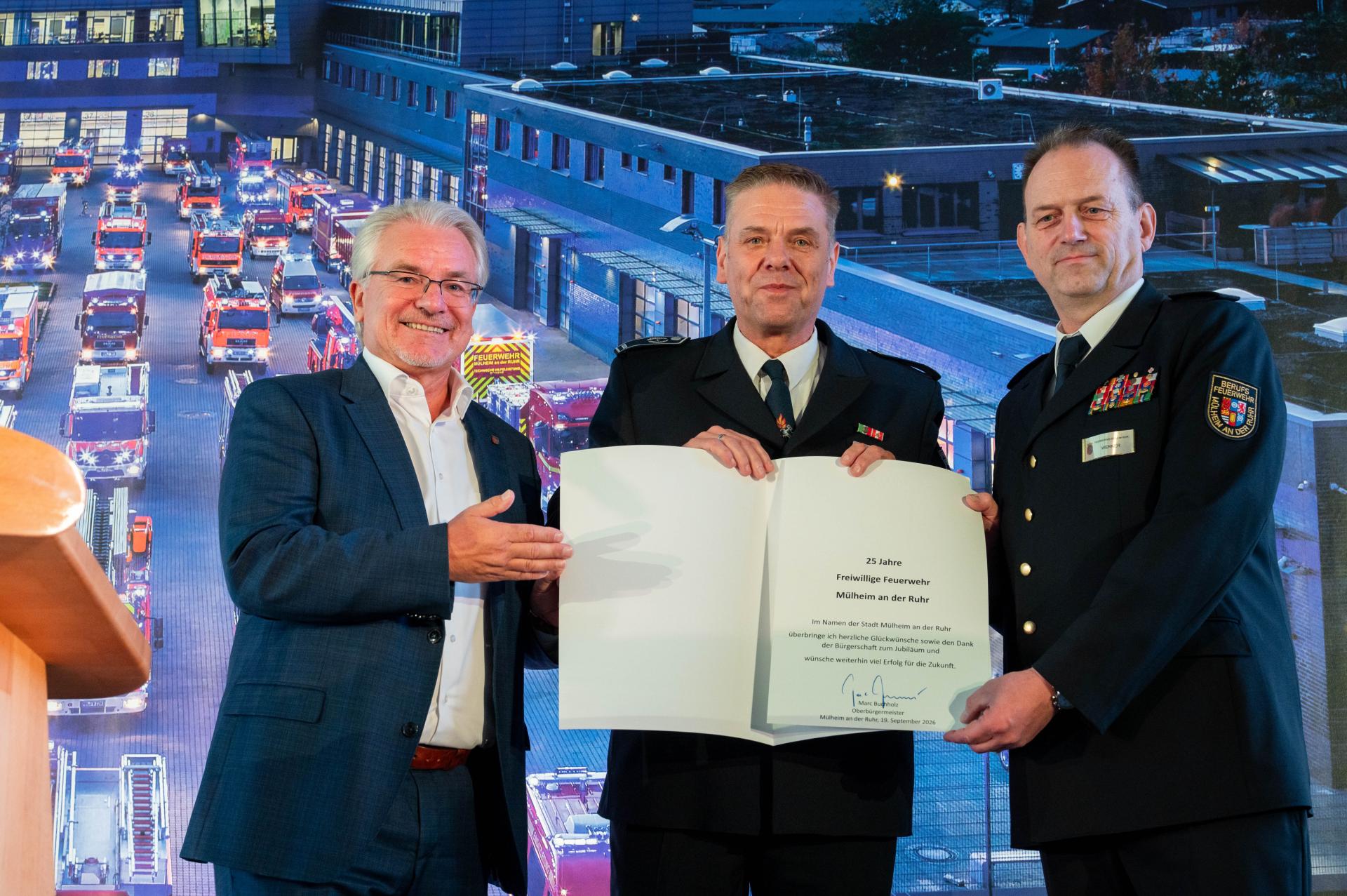 Oberbürgermeister Marc Buchholz überreicht die Jubiläumsurkunde der Stadt an Sven Ratberg und Feuerwehrleiter Sven Werner.
