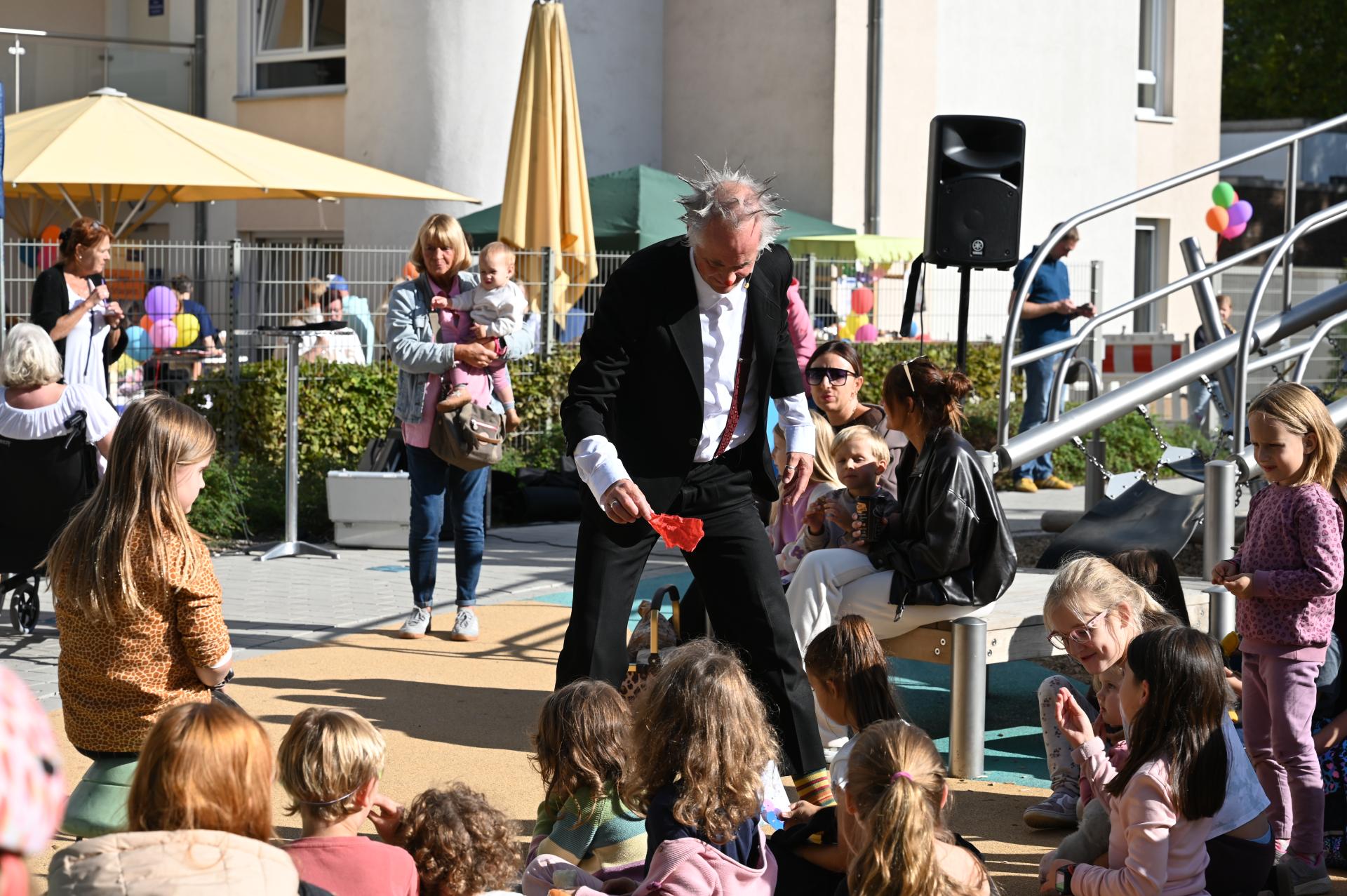 Im Vordergrund sitzen Kinder und sehen sich die Späße von Clown Aki an.
