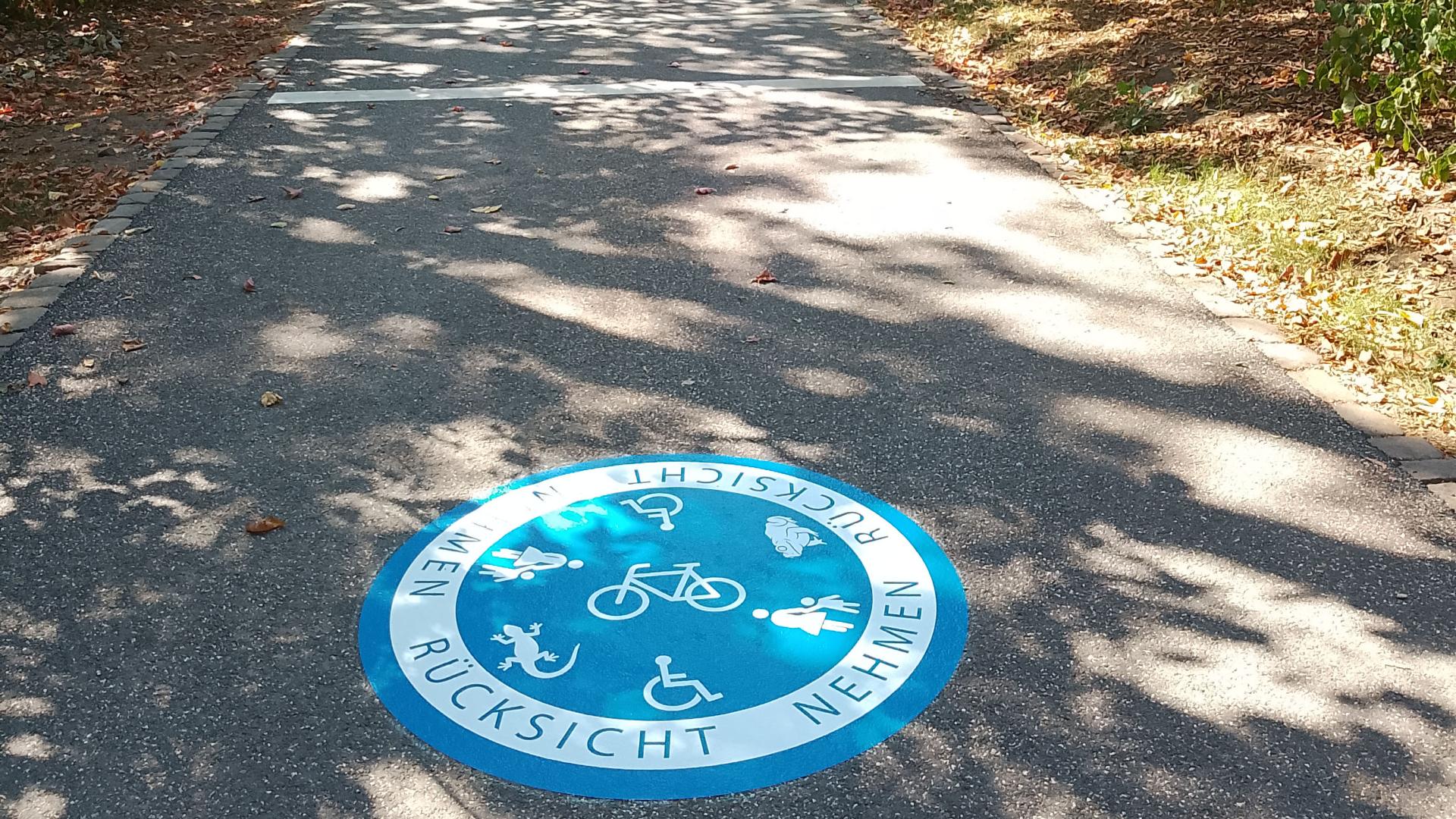 das Foto zeigt einen Hinweisaufkleber auf dem Fossilienweg. Dieser ruft dazu auf Rücksicht zu nehmen auf Fußgänger, Radfahrer, Rollstuhlfahrer, Amphibienwanderung