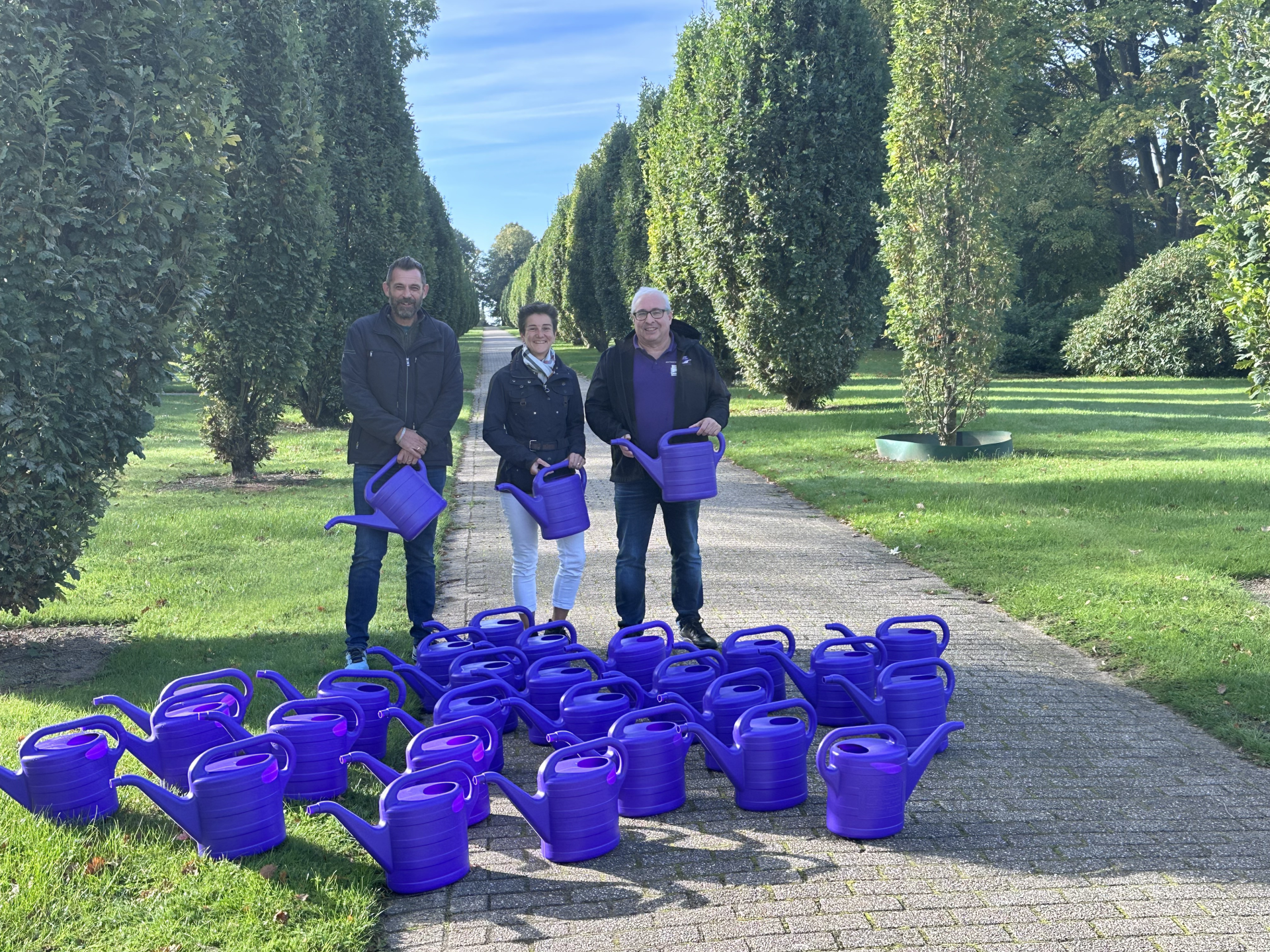 Abteilungsleiterin Friedhöfe Martina Schimanski mit Friedhofsgärtner Dennis Buhle (l.) und Klaus Schneider von der Treuhandstelle Dauergrabpflege, davor die gespendeten violetten Gießkannen